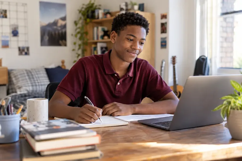 A student writing out working in a notebook beside a laptop